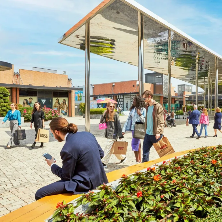 Uomo vestito elegante di spalle seduto sulle panchine in piazza e altre persone che fanno shopping e camminano per il centro