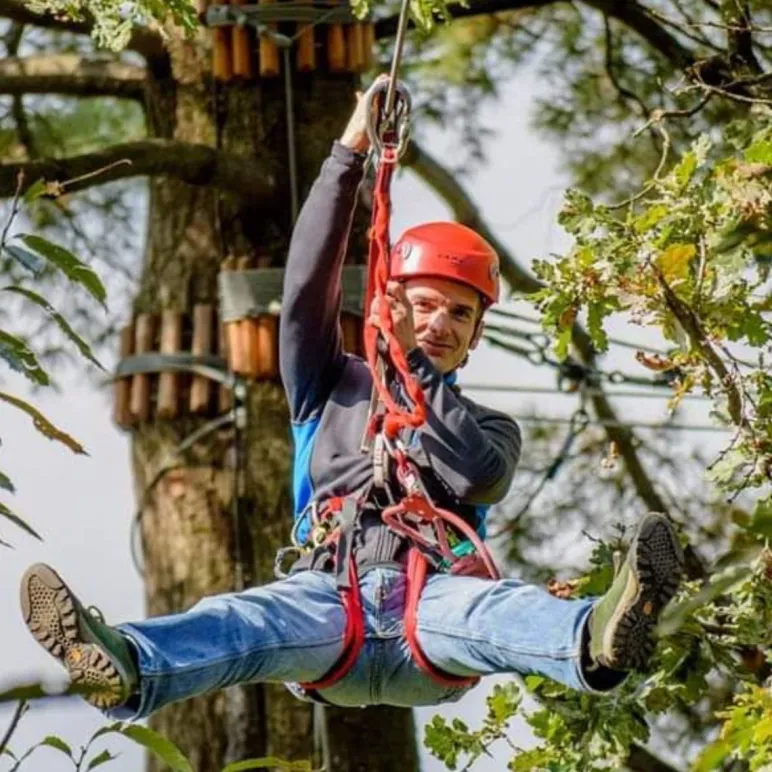 Uomo con imbracatura e caschetto che si sta lanciando con una corda da un albero