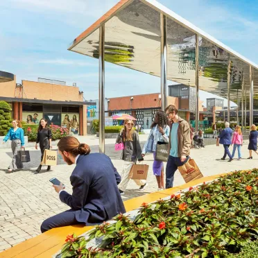 Uomo vestito elegante di spalle seduto sulle panchine in piazza e altre persone che fanno shopping e camminano per il centro